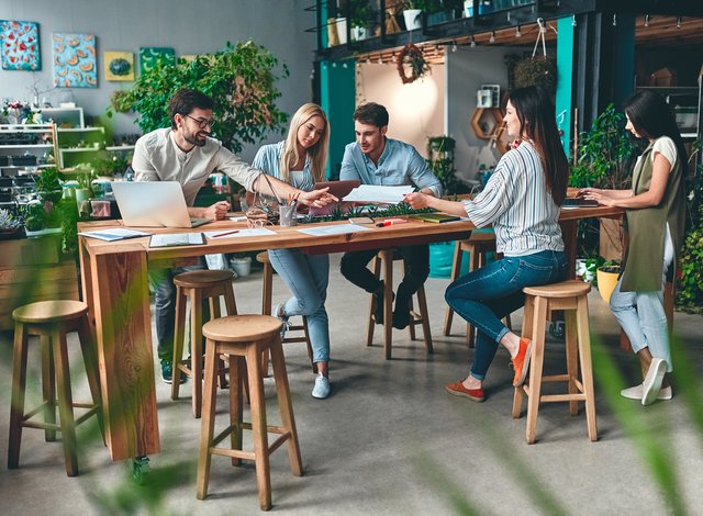 Young co-workers gathered around a table in an office space with green plants